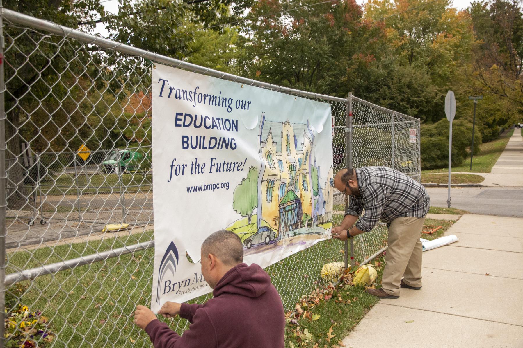 Rich and Howard hang a banner on the fence.